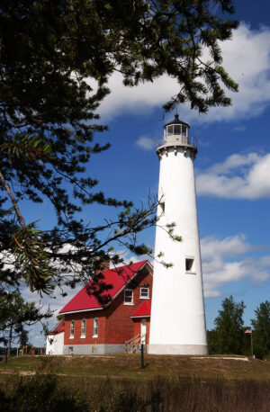 Bright blue skies over a white Michigan lighthouse with red roof, framed by pine branches.