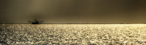 Silhouette of a shrimp boat against the glittering backdrop of the ocean at sunset.