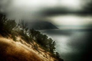 Mist-shrouded dunes overlooking a serene lake captured in "Misty Dune Serenade."