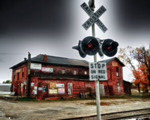 Historic red brick building at a railroad crossing under a dramatic sky, symbolizing the intersection of past and present.