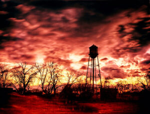 Silhouette of a water tower against a vibrant sunset sky, photographed by Ken Osborne.