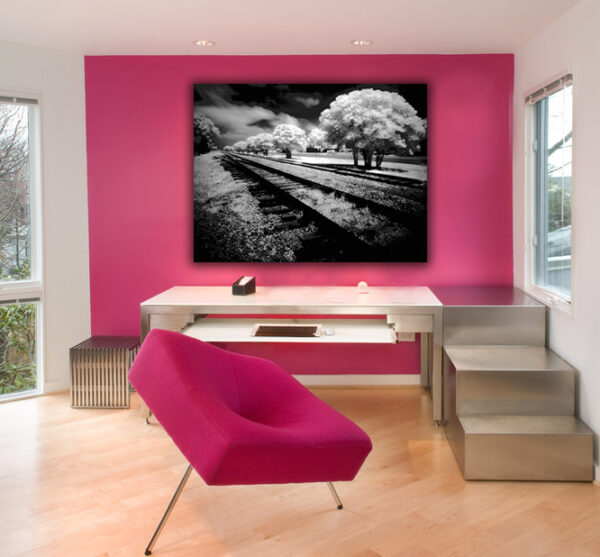 "Ethereal Rails" - An evocative infrared photograph of railroad tracks under a dramatic sky, juxtaposed against a vibrant fuchsia wall in a modern workspace.